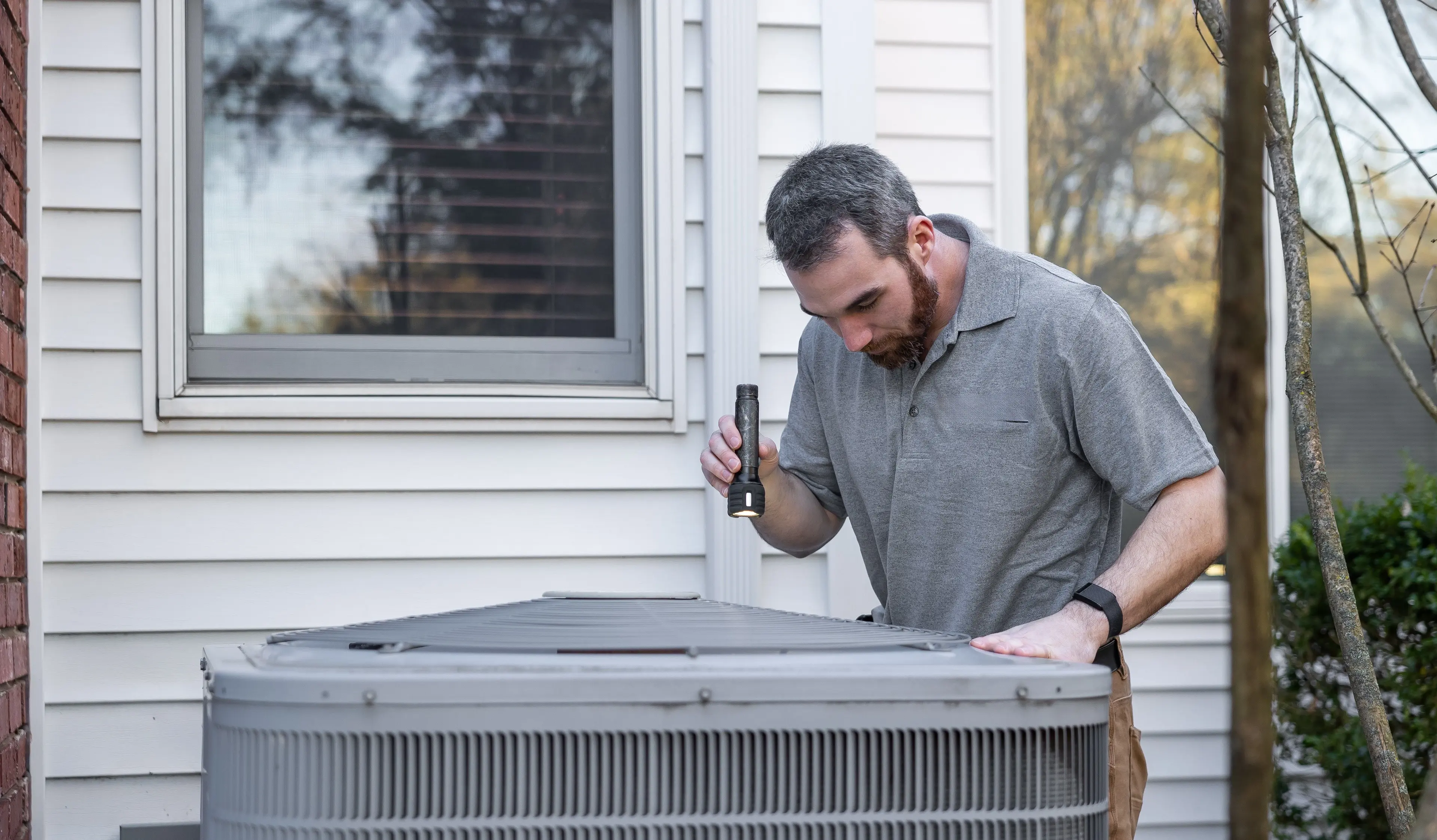 Technician checking an outdoor AC unit beside an older home